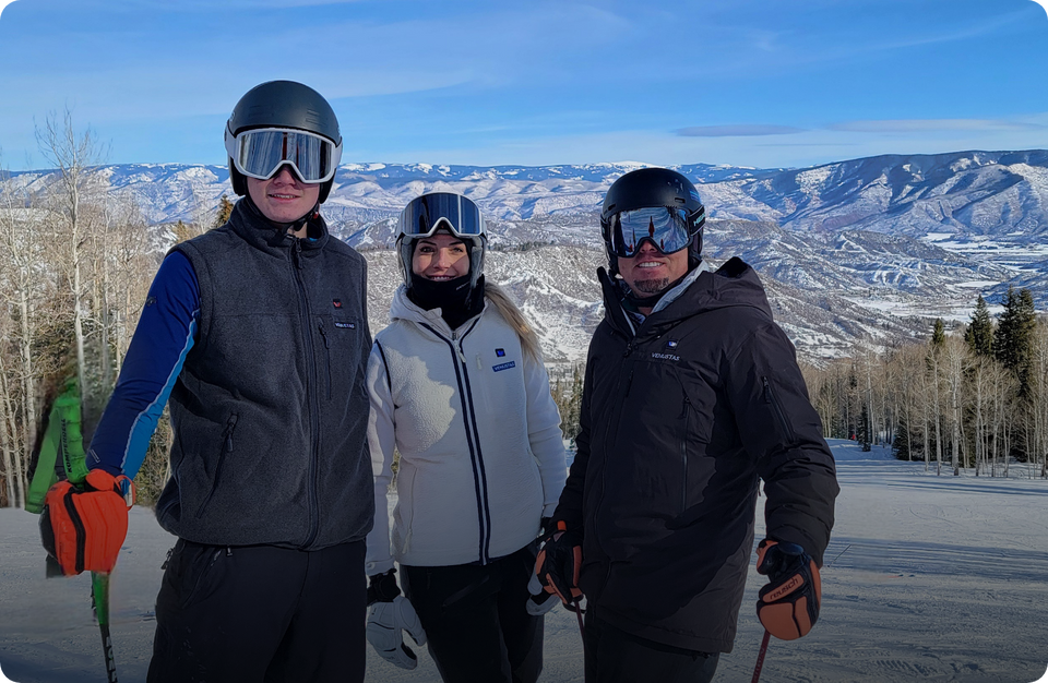 Three people in ski gear standing on a snowy slope with mountains in the background