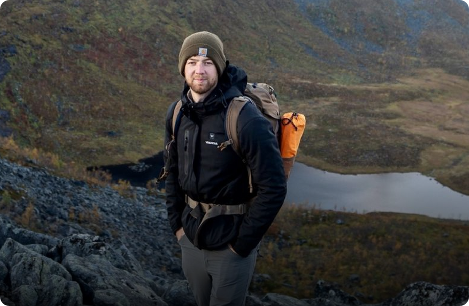 Man with a backpack standing on a mountain with a lake in the background