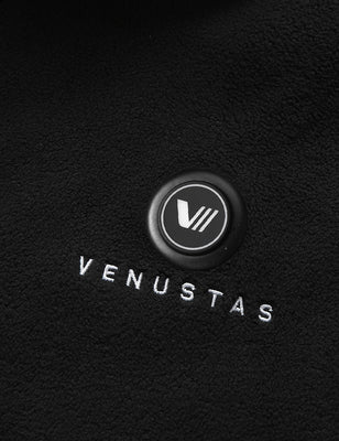 Black heated fleece vest close-up showing the chest power button and embroidered logo