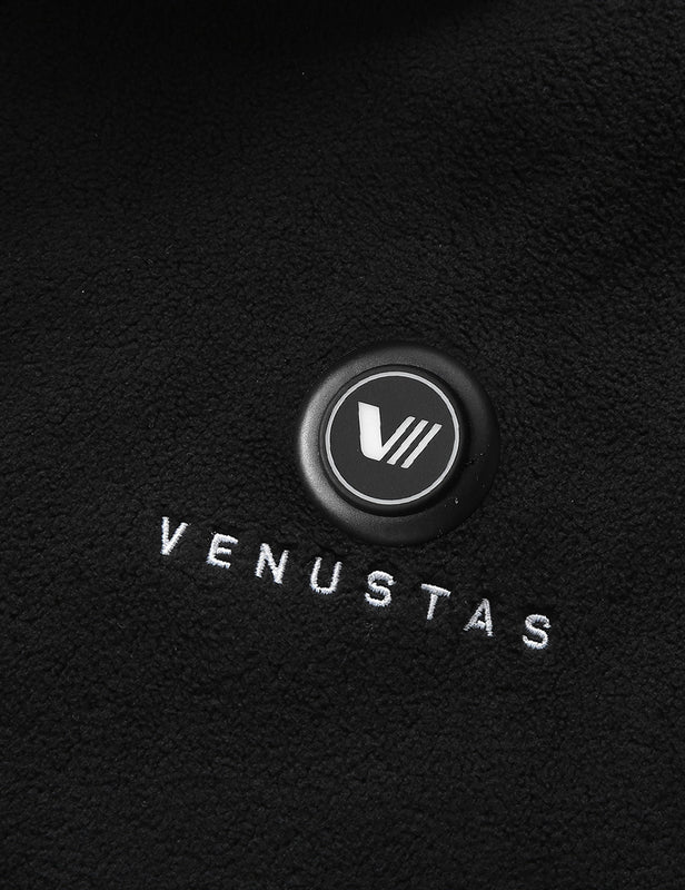 Black heated fleece vest close-up showing the chest power button and embroidered logo