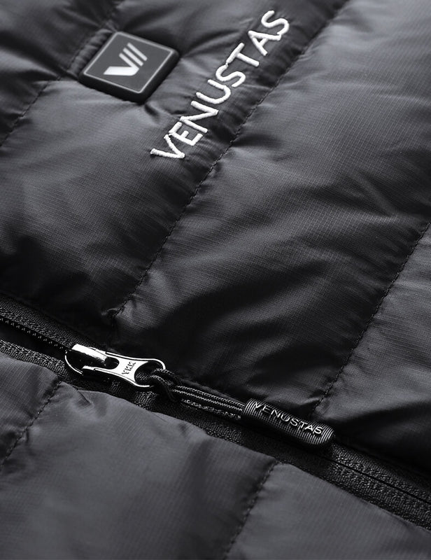 Close-up of black heated vest showing zipper pull, logo embroidery, and power button
