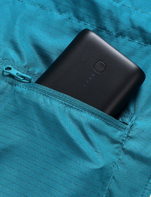 Black battery pack tucked into a teal heated vest zipper pocket